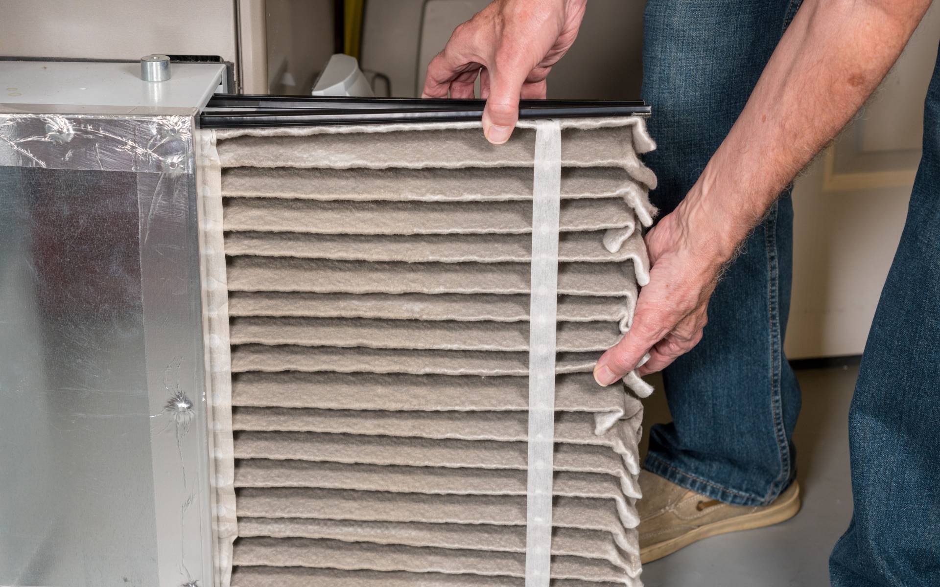 A man replacing a dirty HVAC air filter inside a furnace system