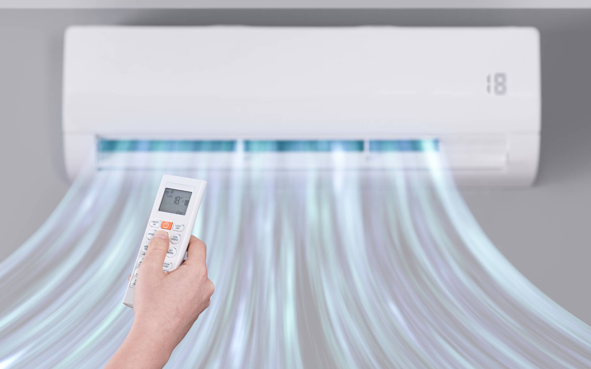 Hand holding a remote to control a wall-mounted ductless mini-split air conditioner blowing cool air