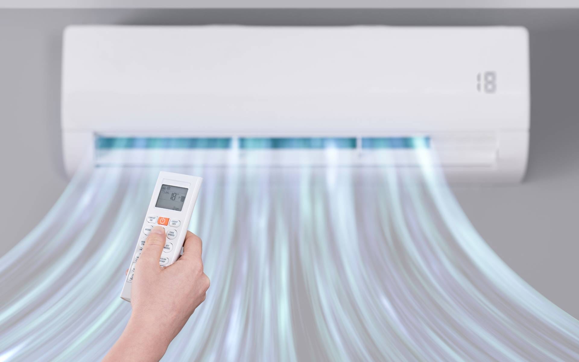 Hand holding a remote to control a wall-mounted ductless mini-split air conditioner blowing cool air