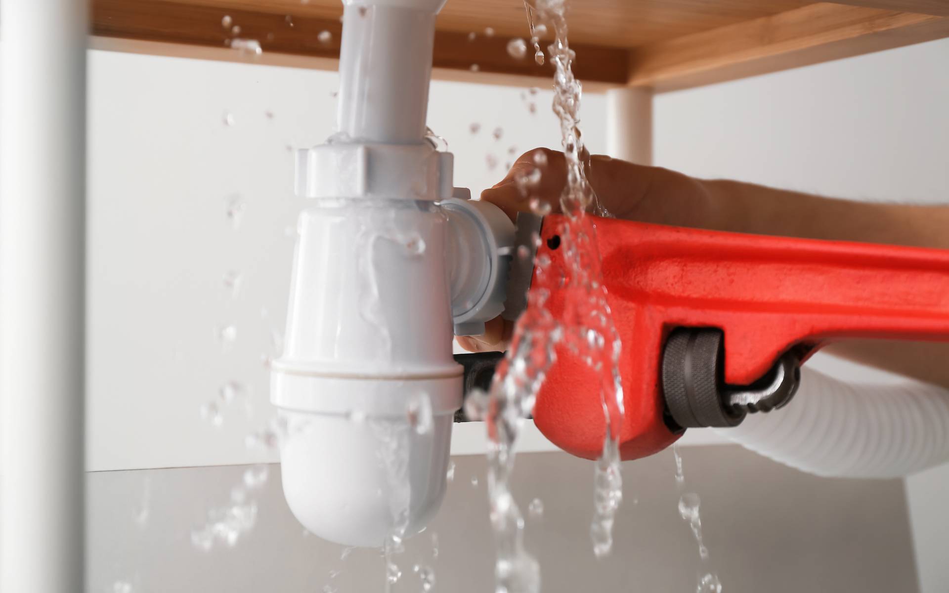 Plumber fixing leaking pipe under sink with red pipe wrench