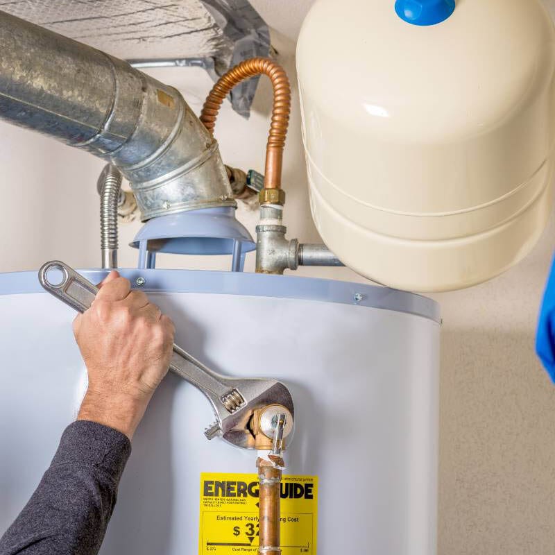Technician using wrench to service a residential water heater