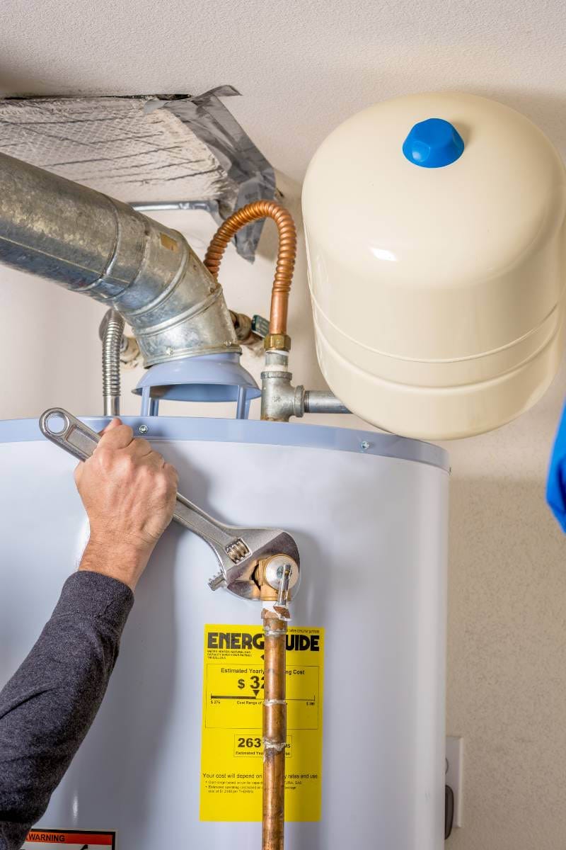 Technician using wrench to service a residential water heater
