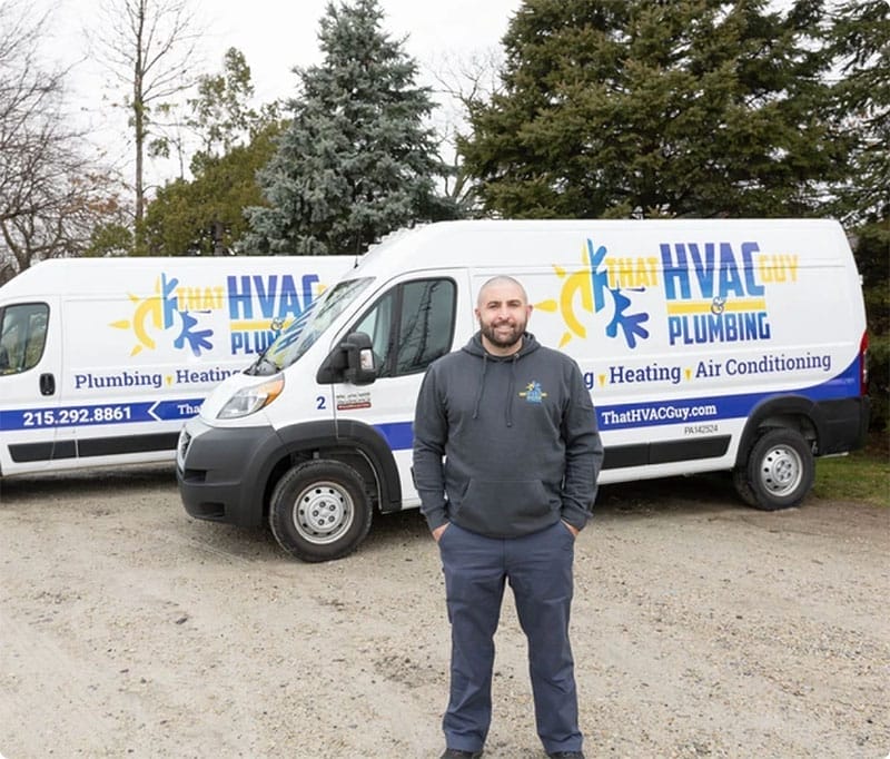 HVAC technician standing in front of service vans of That HVAC Guy & Plumbing