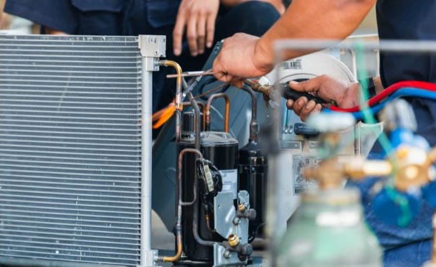 Technician performing HVAC repair by working on air conditioning unit components with tools and gauges