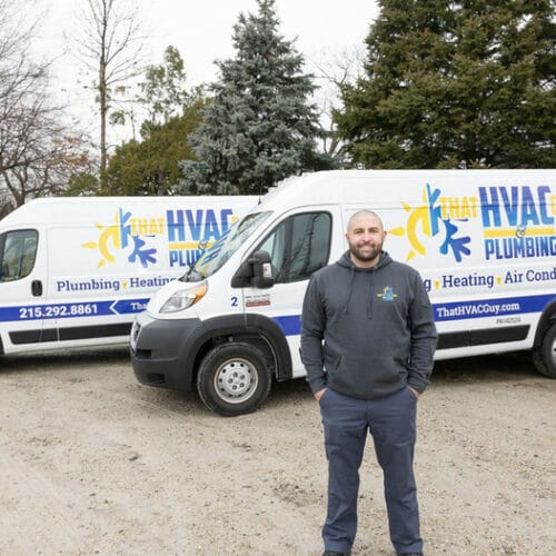 HVAC technician standing in front of service vans of That HVAC Guy & Plumbing