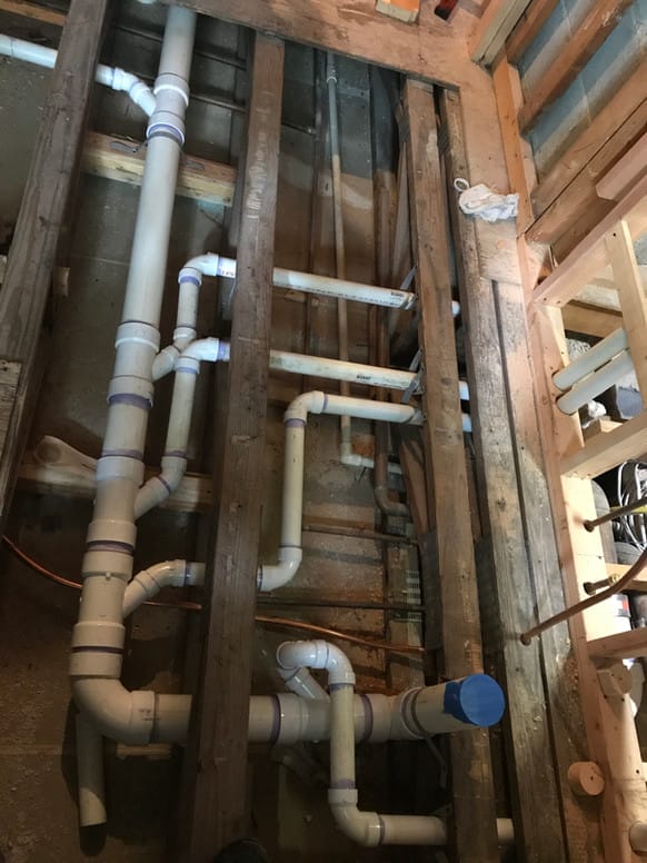 Exposed framing with newly installed PVC plumbing lines between floor joists