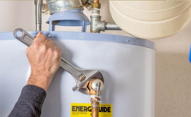 Technician using wrench to service a residential water heater