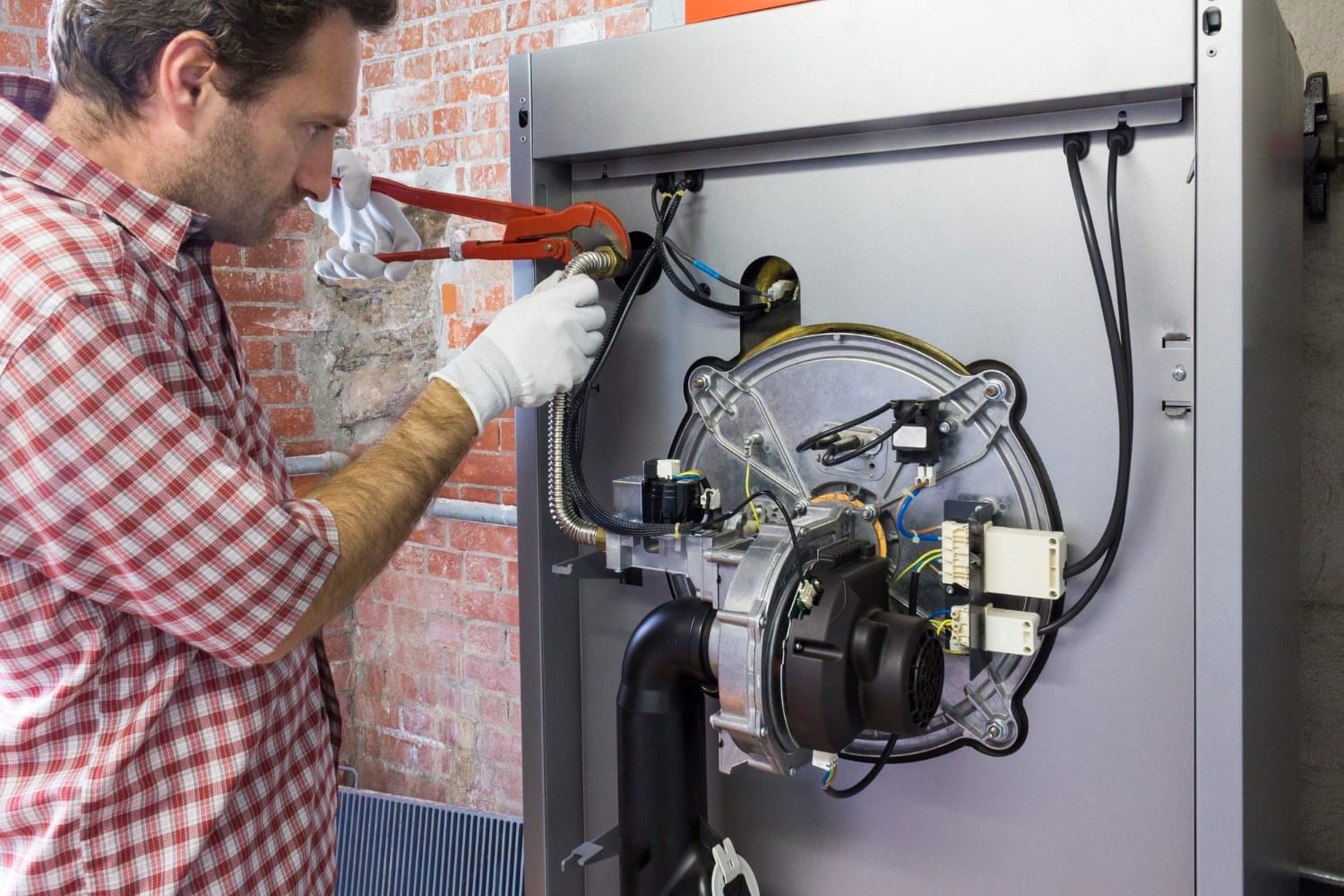 A repairman wearing a uniform and safety gloves is focused on fixing a machine furnace, using a wrench to adjust components.